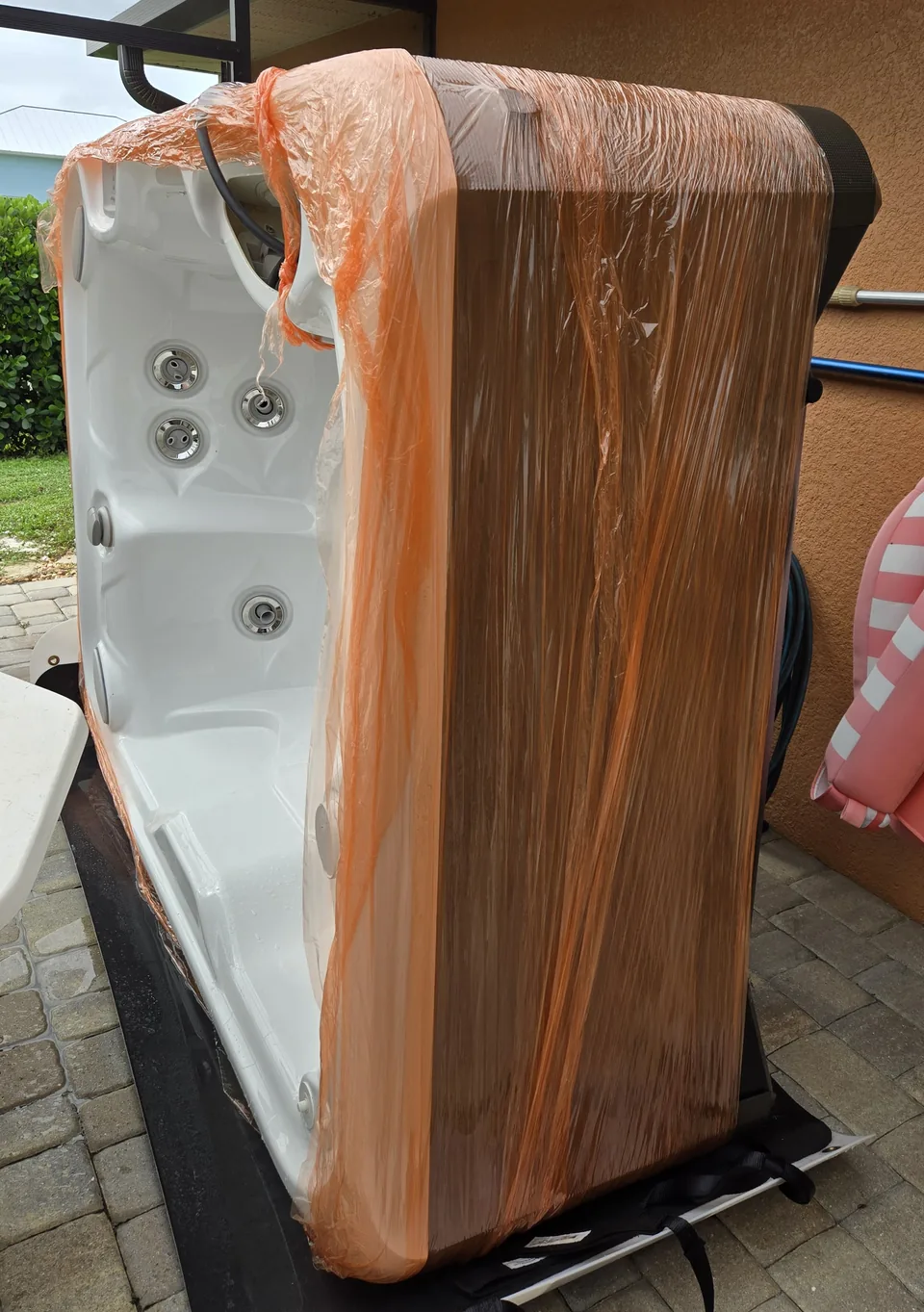 Wrapped hot tub positioned upright on moving equipment inside a screened patio.