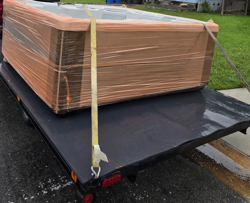 Wrapped hot tub and tie-down strap on a trailer.